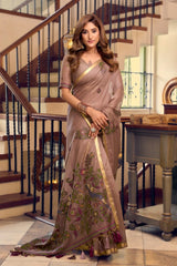 Woman in a brown saree with floral patterns standing in a home setting.