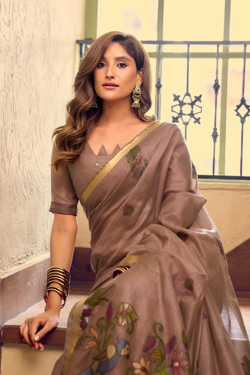 Woman wearing a brown saree with floral patterns indoors.