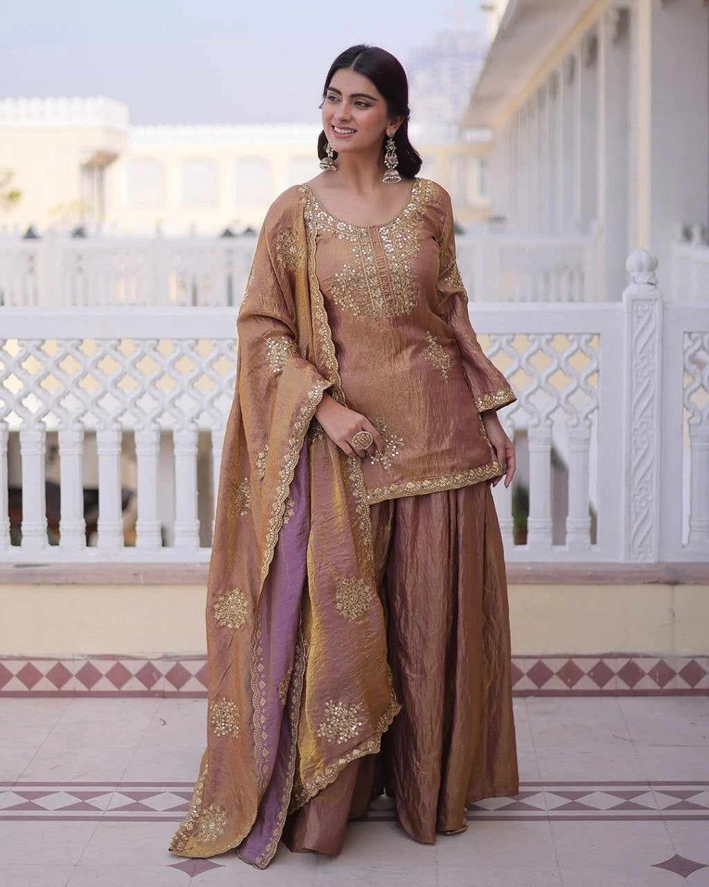 Woman in a traditional brown outfit with gold embroidery standing on a balcony.
