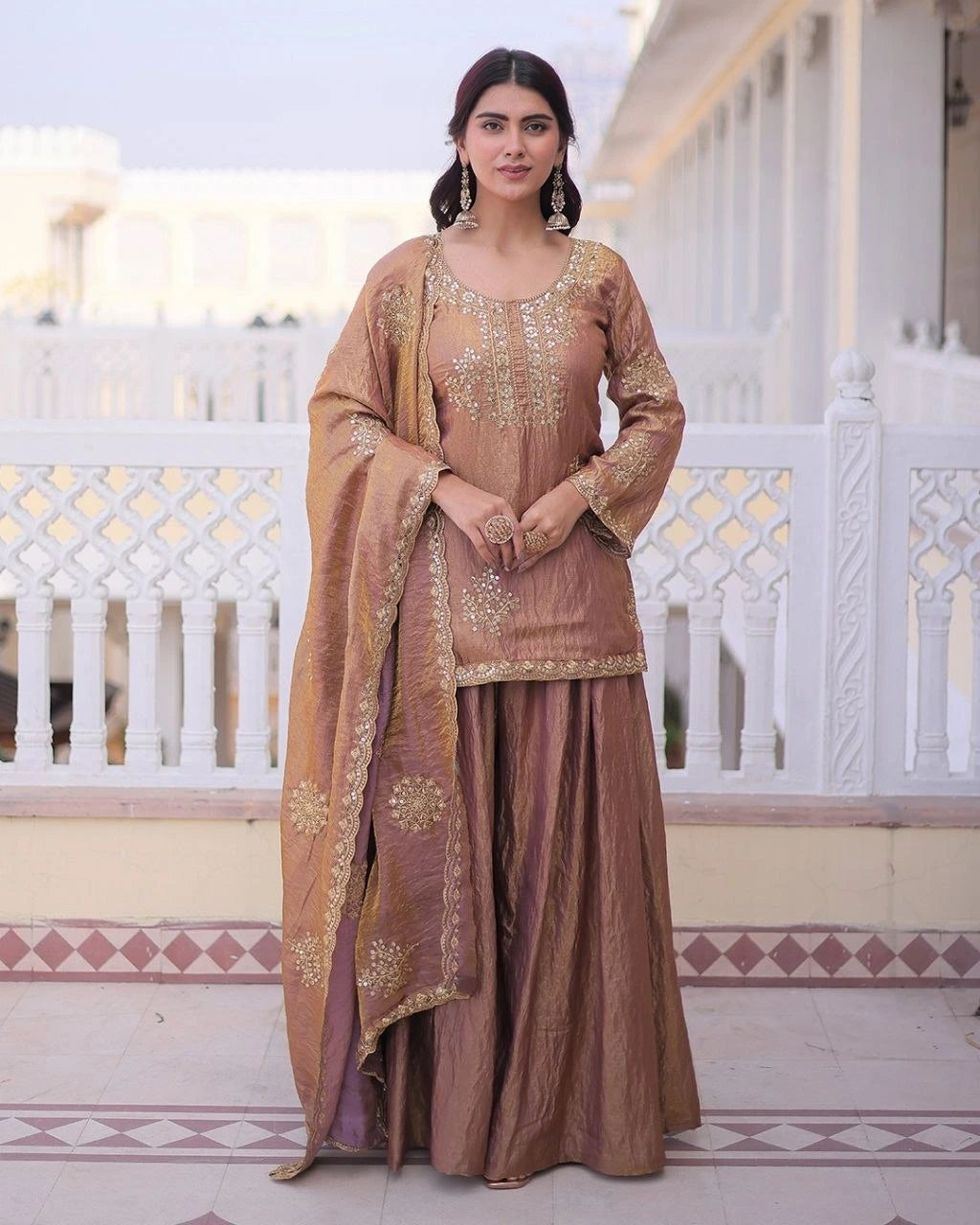 Woman in a traditional brown outfit with gold embroidery standing on a decorative floor.