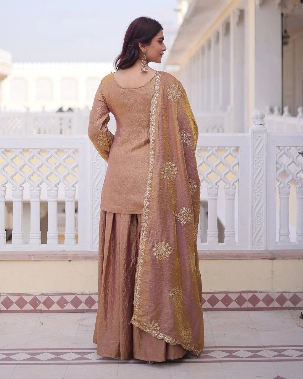 Woman in a traditional outfit standing on a balcony with white railings and decorative tiles.