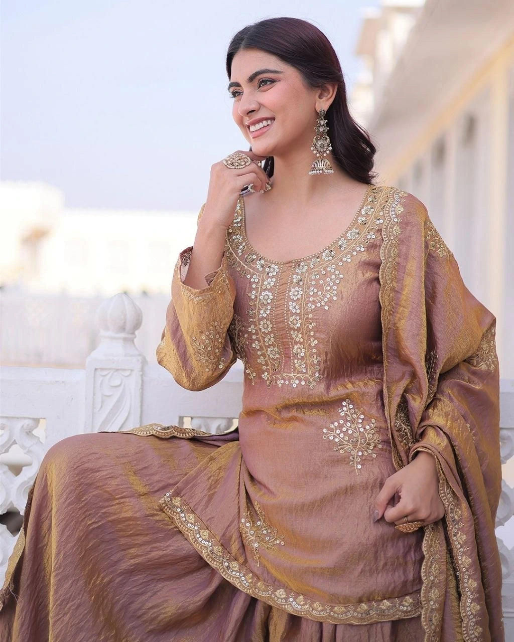 Woman in a traditional outfit with gold embroidery sitting on a white bench.