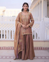 Woman in a traditional brown outfit with gold embroidery standing on a decorative floor.