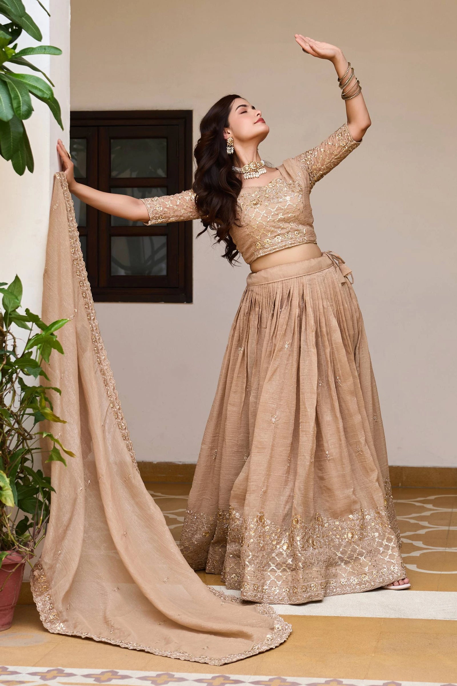 Woman in a traditional beige outfit with a matching dupatta, posing indoors.