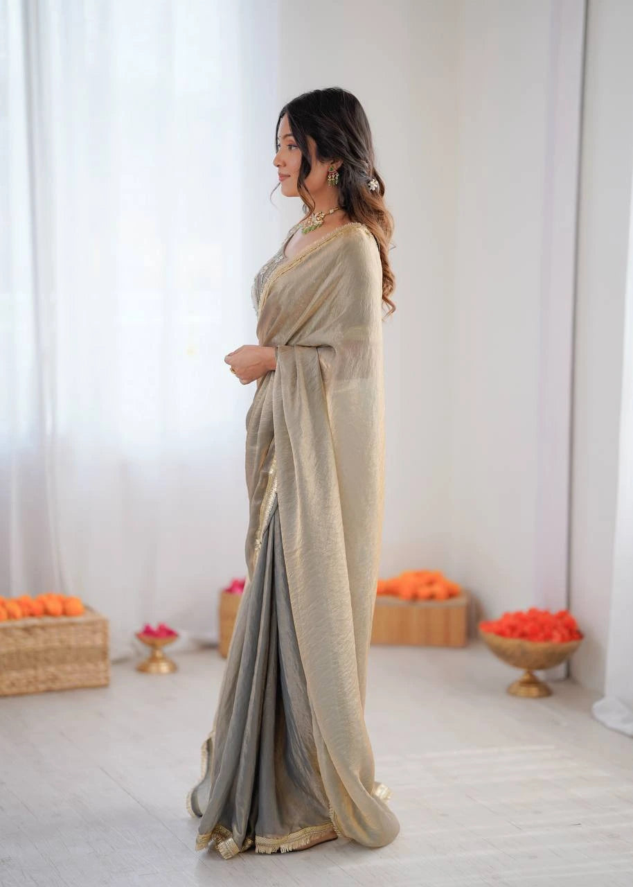 Woman in a beige and gray saree standing in a minimalistic room with decorative elements.