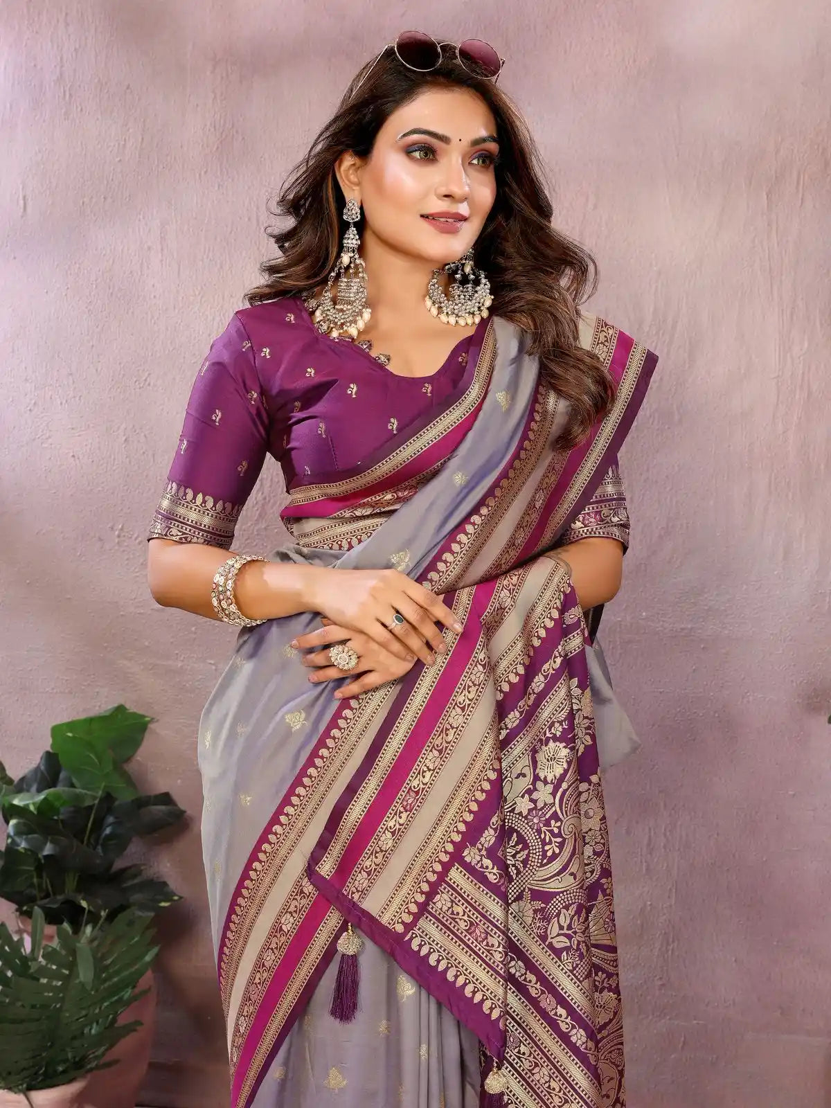 Woman wearing a purple and gray saree with gold patterns against a neutral background