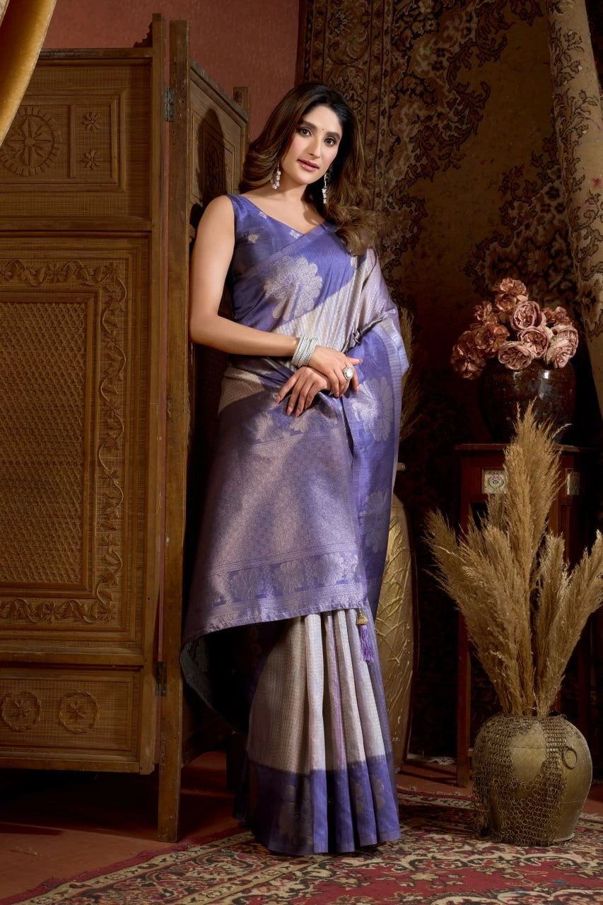 Woman in a traditional saree standing in a decorated room with wooden furniture and floral decorations.