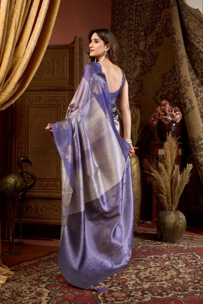 Woman in a purple saree standing in an ornate room with decorative curtains and decor.