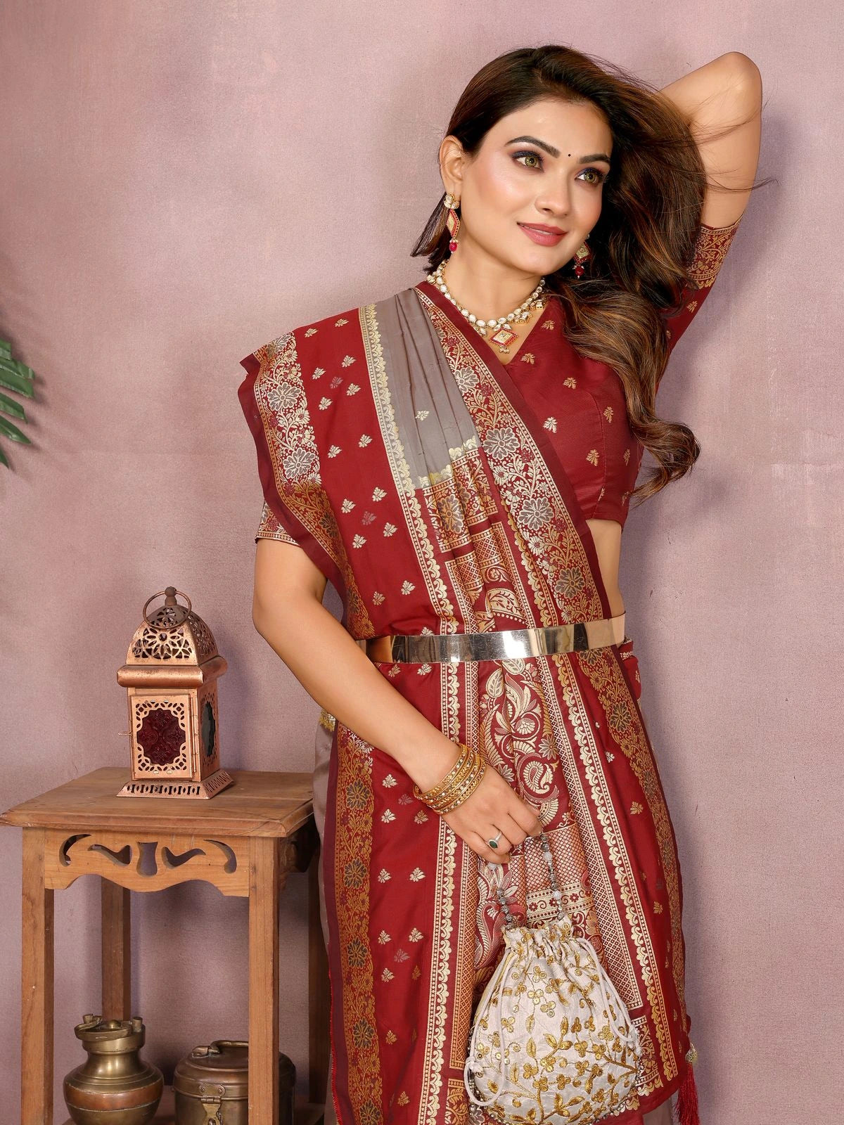 Woman in a red saree with gold patterns against a pink background