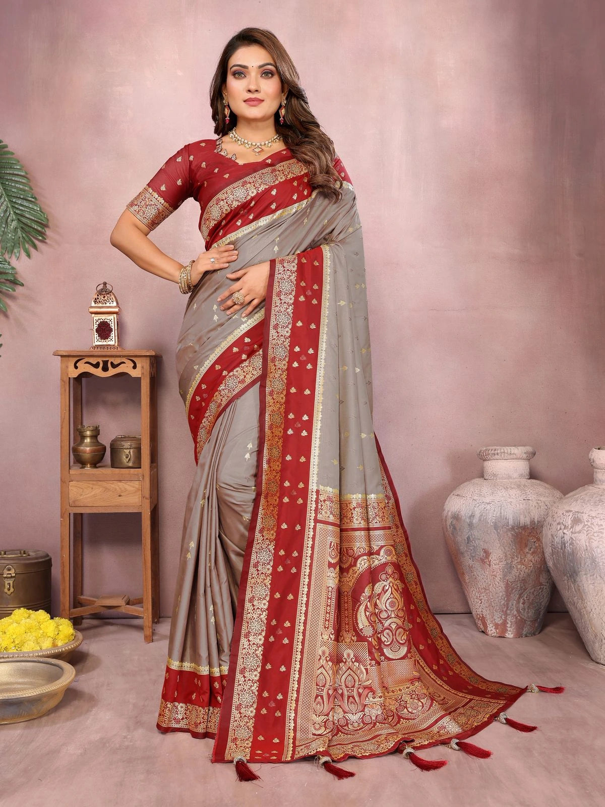 Woman wearing a red and gray saree with gold patterns in a decorated room.