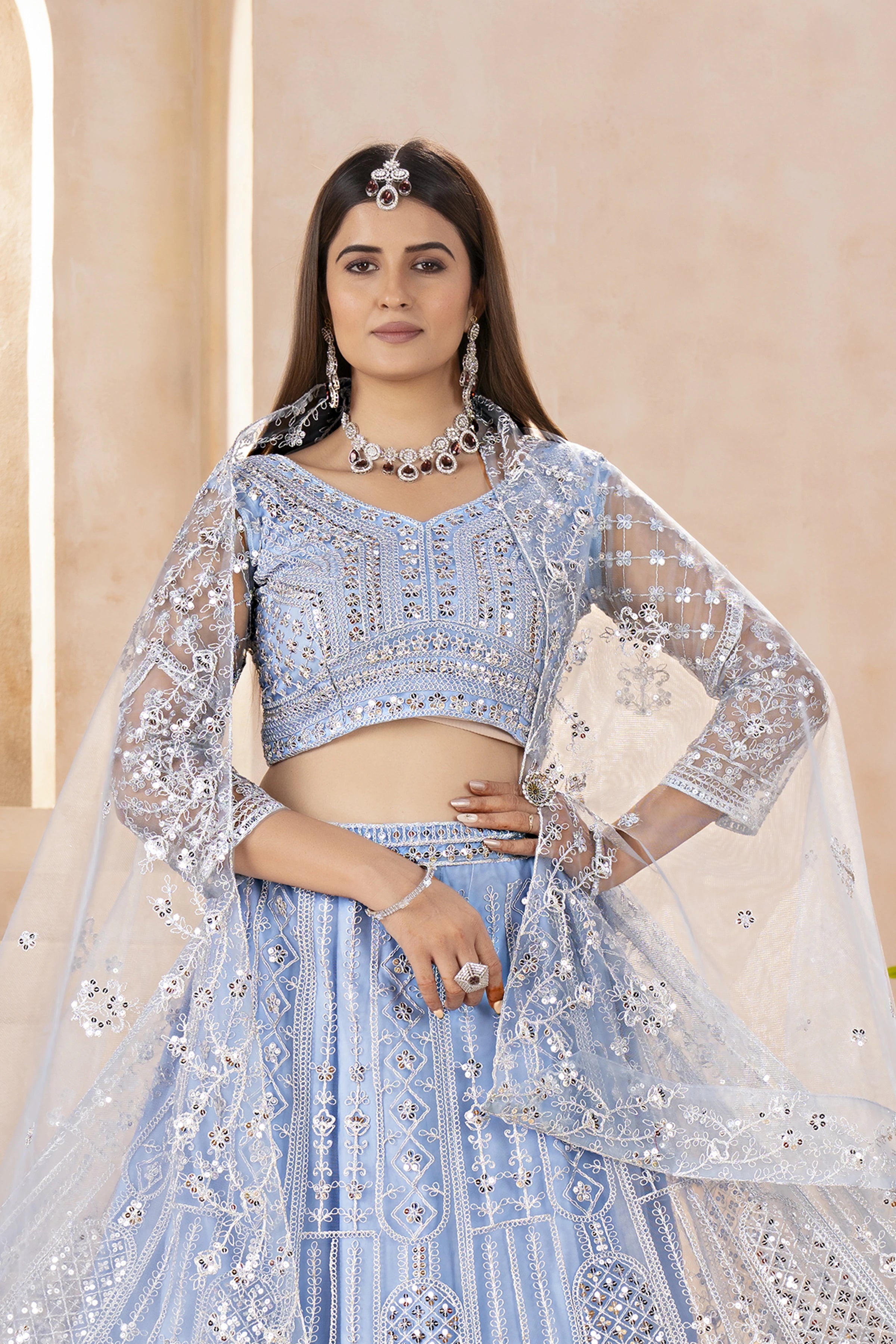 Woman wearing a light blue embroidered lehenga with silver details against a beige background