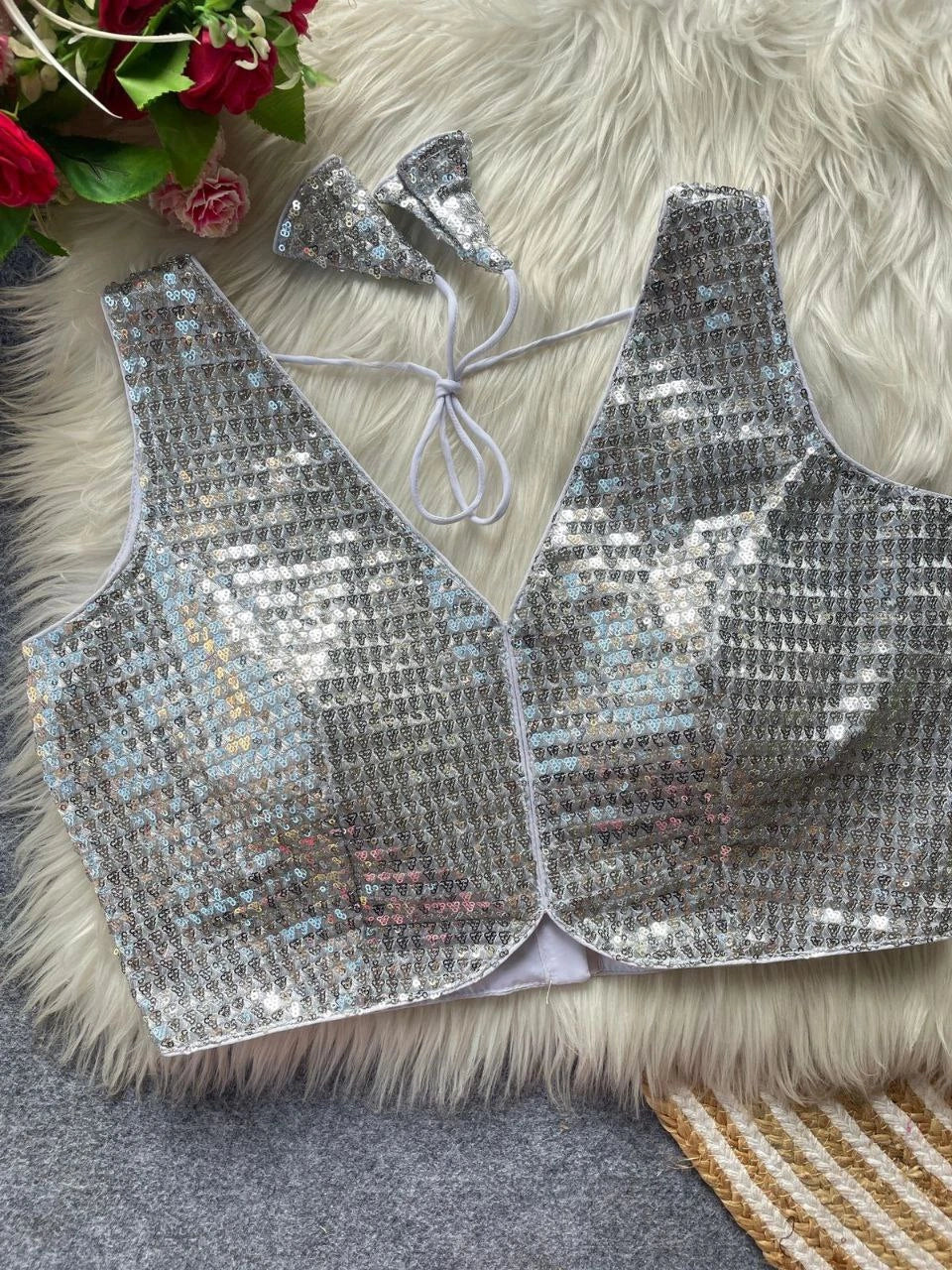 Silver sequin top on a fluffy white surface with flowers in the corner.