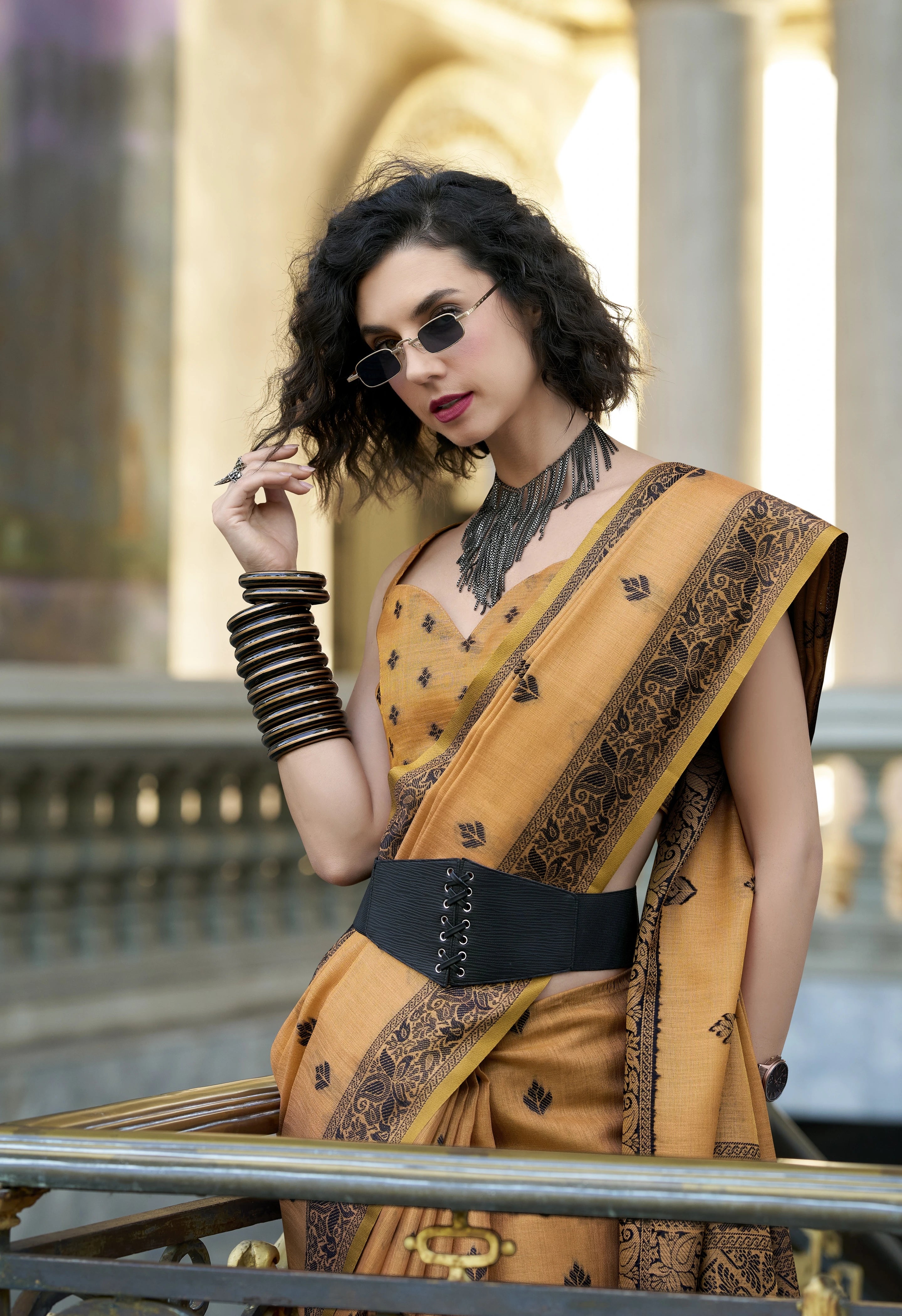 Woman in a mustard yellow saree with intricate patterns, standing outdoors.
