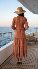 Woman in a long dress and hat standing on a yacht deck overlooking the ocean.