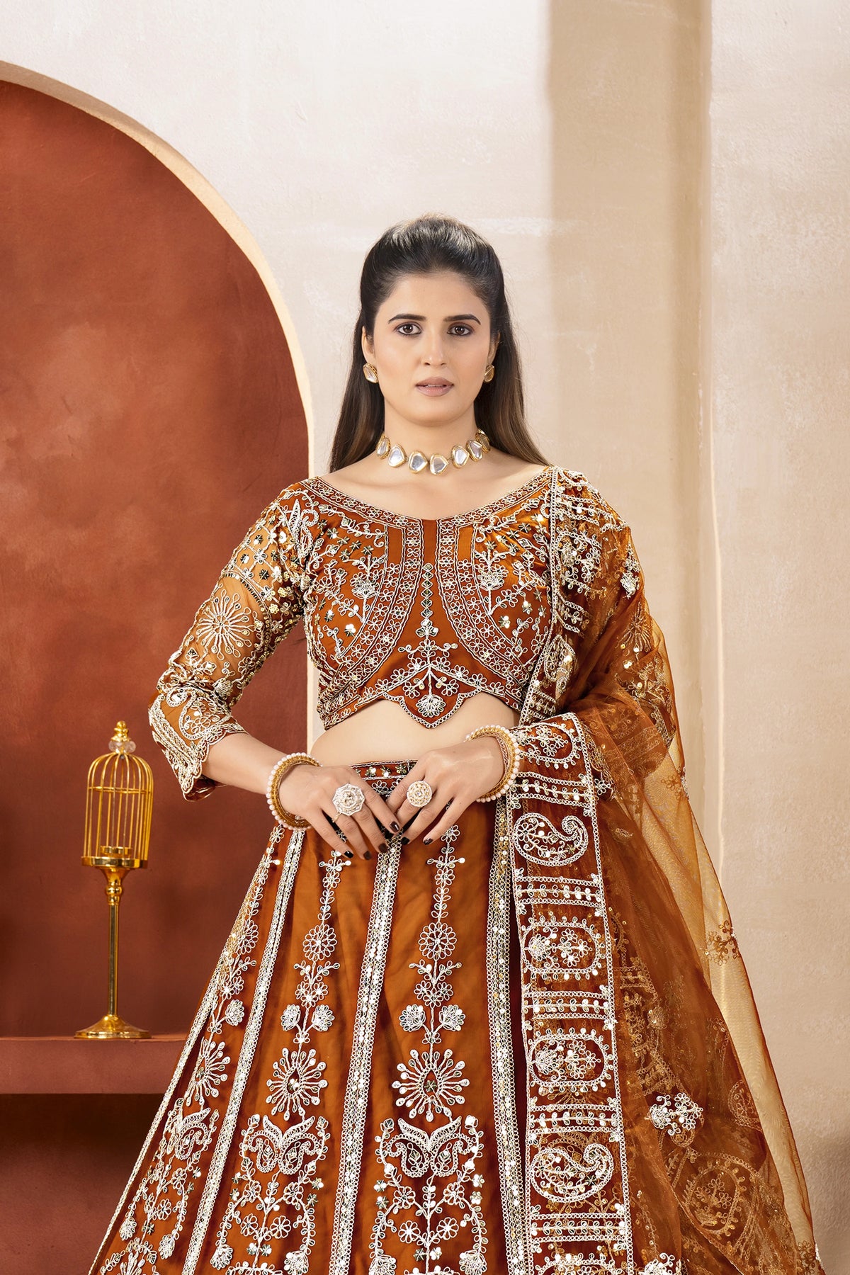 Woman in an orange and gold embroidered traditional outfit with a decorative background