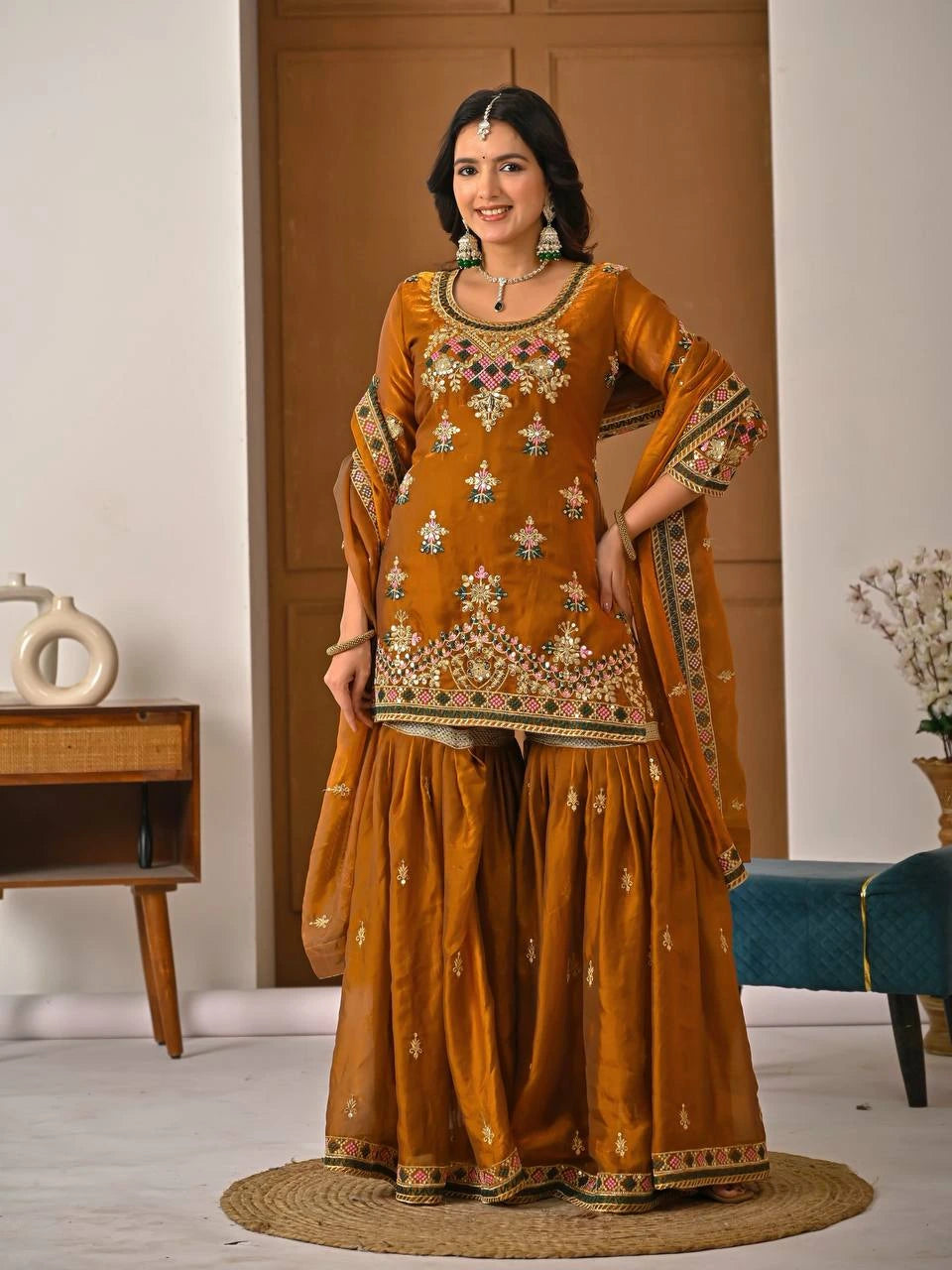 Woman in a mustard yellow traditional outfit with intricate patterns in a room.