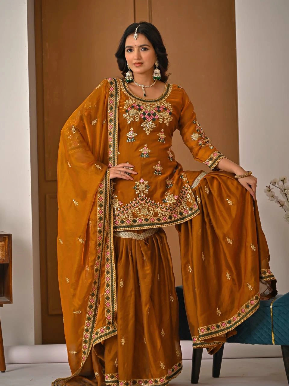 Woman in a traditional mustard yellow outfit with intricate embroidery indoors.