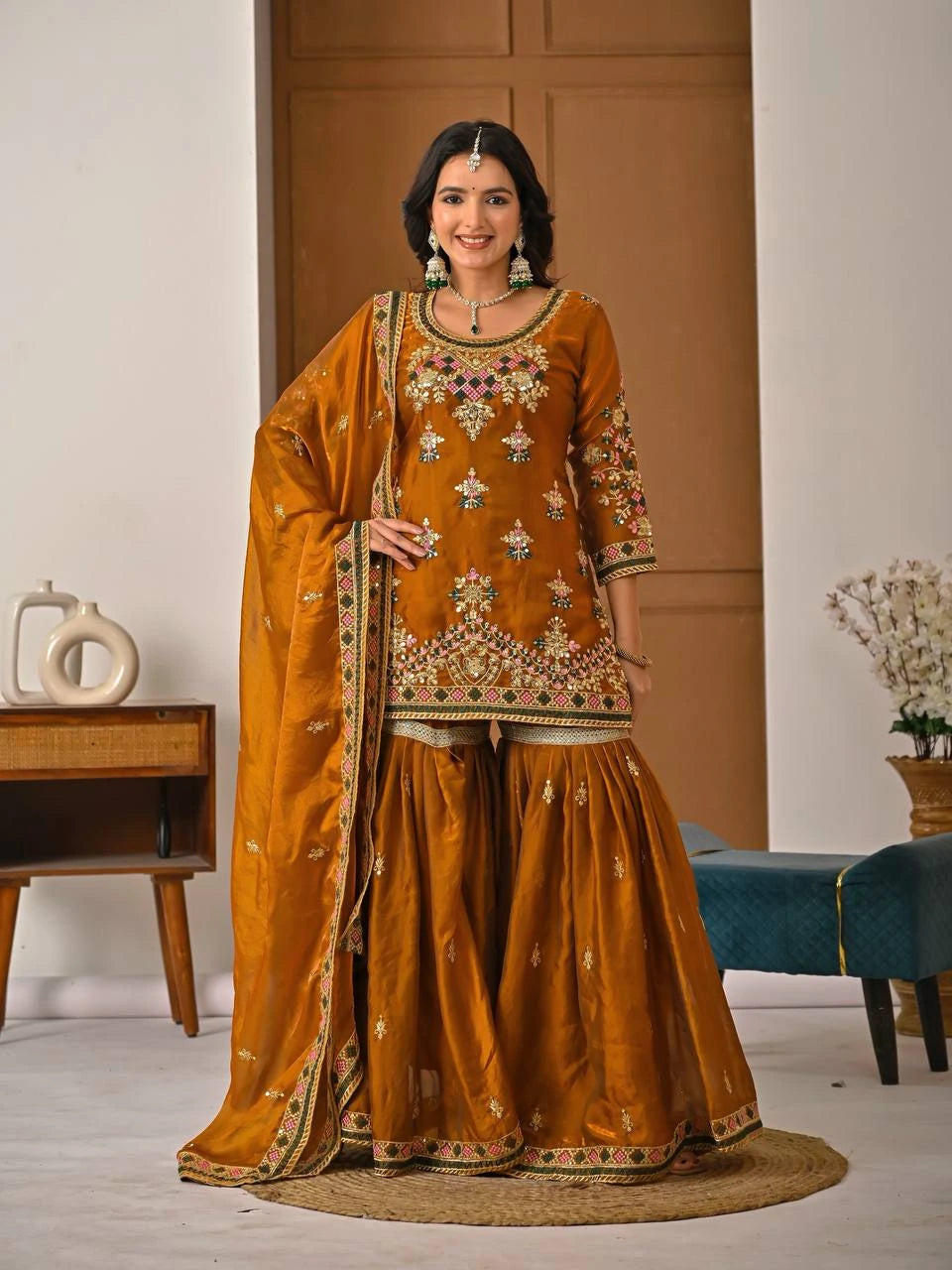 Woman in a traditional mustard yellow embroidered outfit standing indoors.