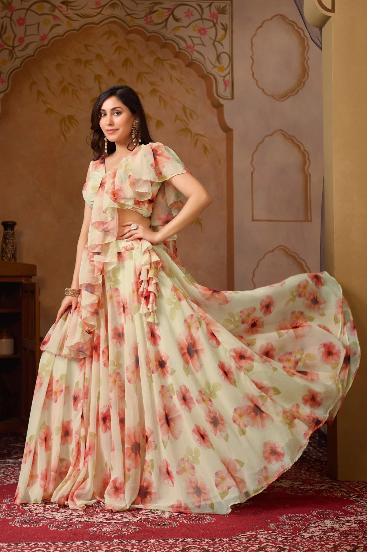 Woman in a floral saree standing in a decorated room with an archway.