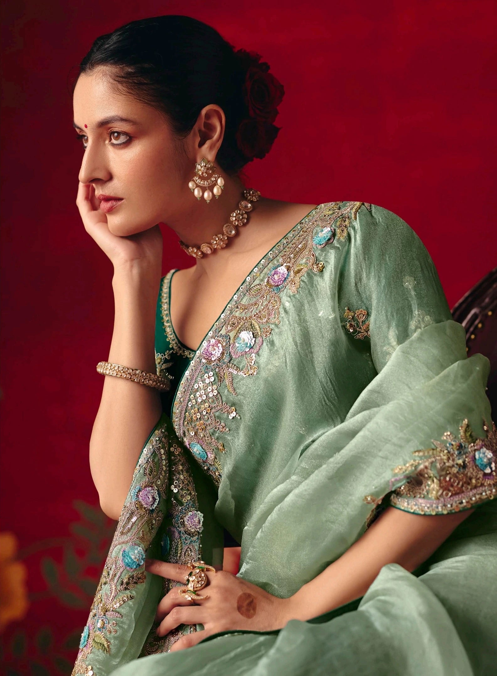 Woman in a traditional green saree with intricate patterns against a red background