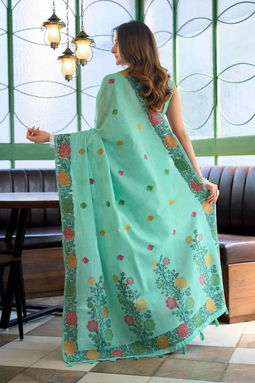 Woman holding a light blue saree with floral patterns in a room with green walls and a window.