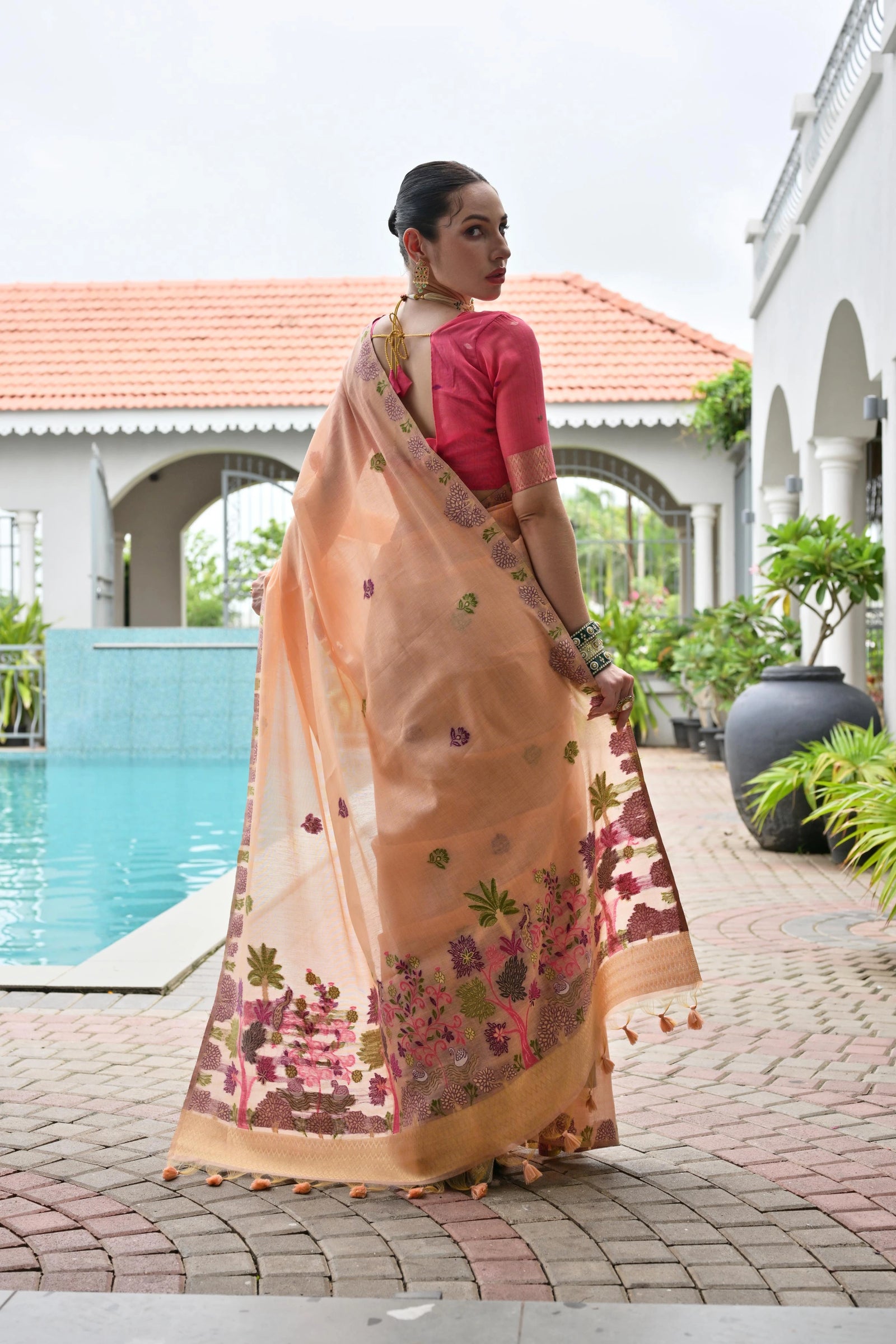 Woman in a peach saree with floral patterns standing by a poolside.