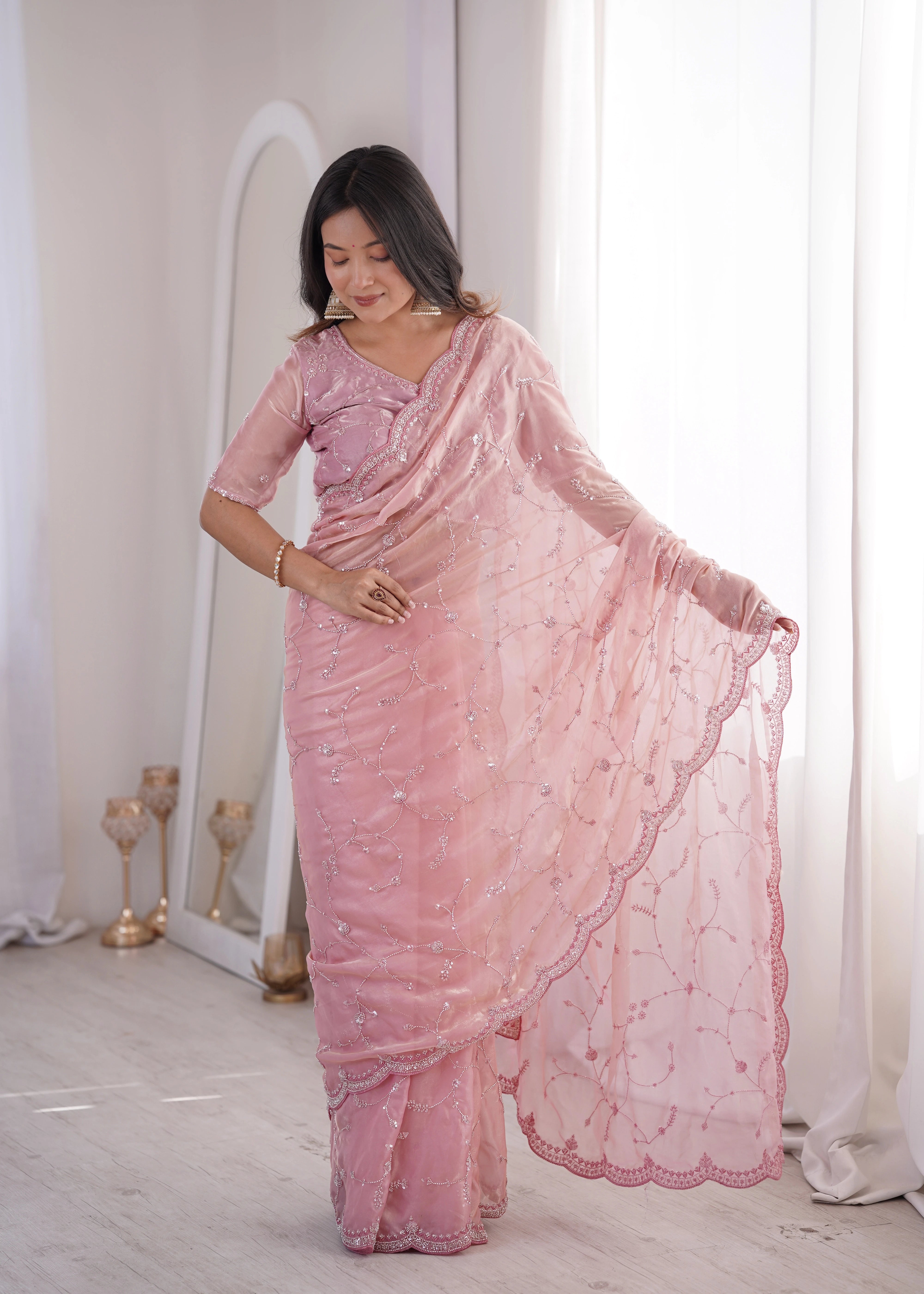 Woman wearing a pink saree in a room with white walls and a mirror.
