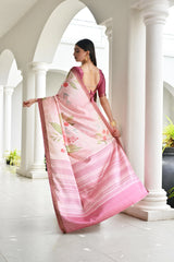 Woman in a pink saree with floral patterns standing in a white architectural setting.