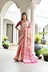 Woman in a pink saree with floral patterns standing in an elegant outdoor setting.