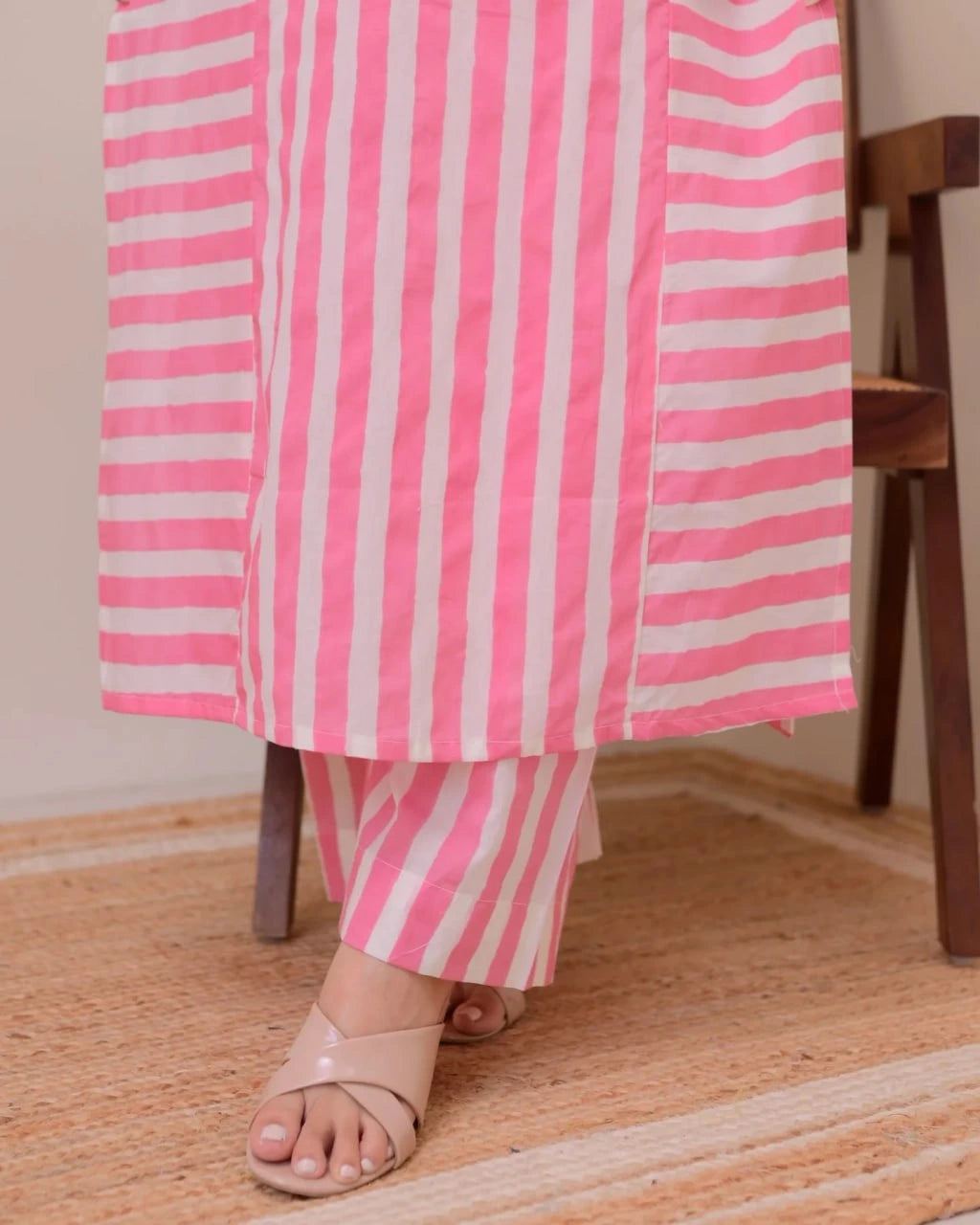 Person wearing a pink and white striped outfit sitting on a wooden chair.