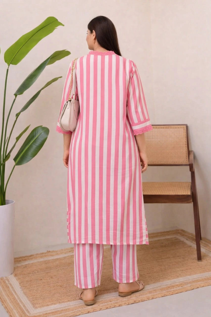 Woman wearing a pink and white striped outfit standing in a room with a plant and chair.