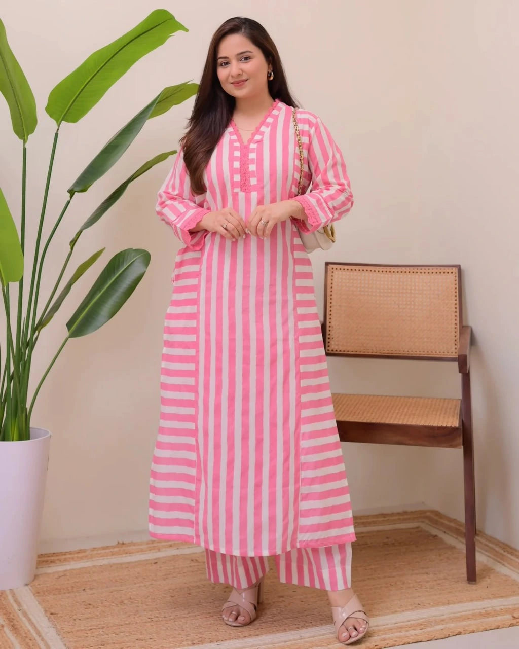 Woman wearing a pink and white striped outfit standing in a room with a plant and chair.