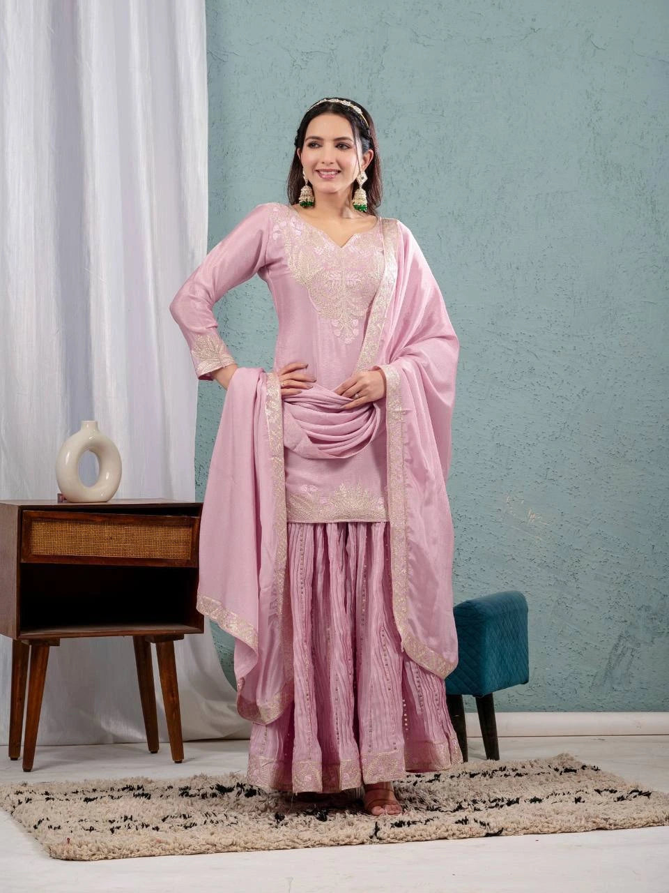 Woman in a pink traditional outfit standing in a room with a light blue wall and white curtains.