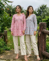 Two women wearing matching outfits with a heart pattern in a garden setting.