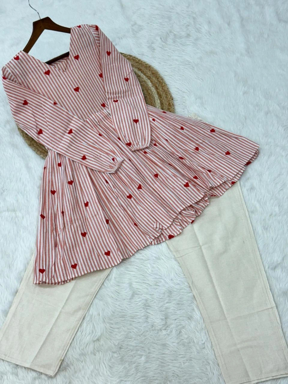 Pink and white striped dress with red heart patterns on a textured surface