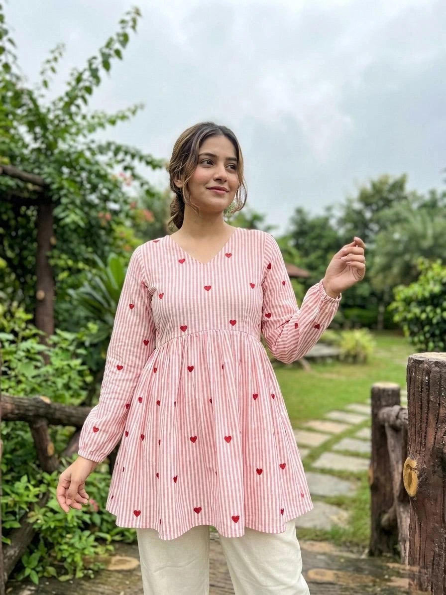Woman wearing a pink and white striped top with red heart patterns in a garden setting