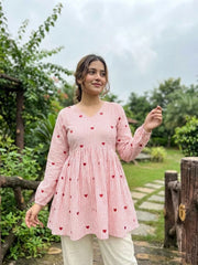 Woman wearing a pink and white striped top with red heart patterns in a garden setting