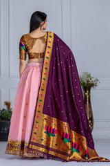Woman wearing a traditional outfit with a purple dupatta and pink skirt against a white wall.