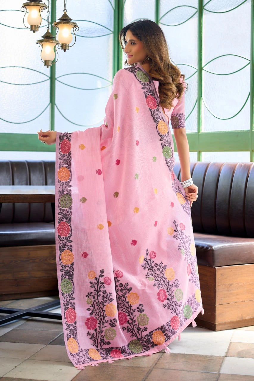 Woman wearing a pink saree with floral patterns in a room with green walls and a brown sofa.