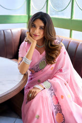Woman in a pink saree sitting on a couch with a blurred background