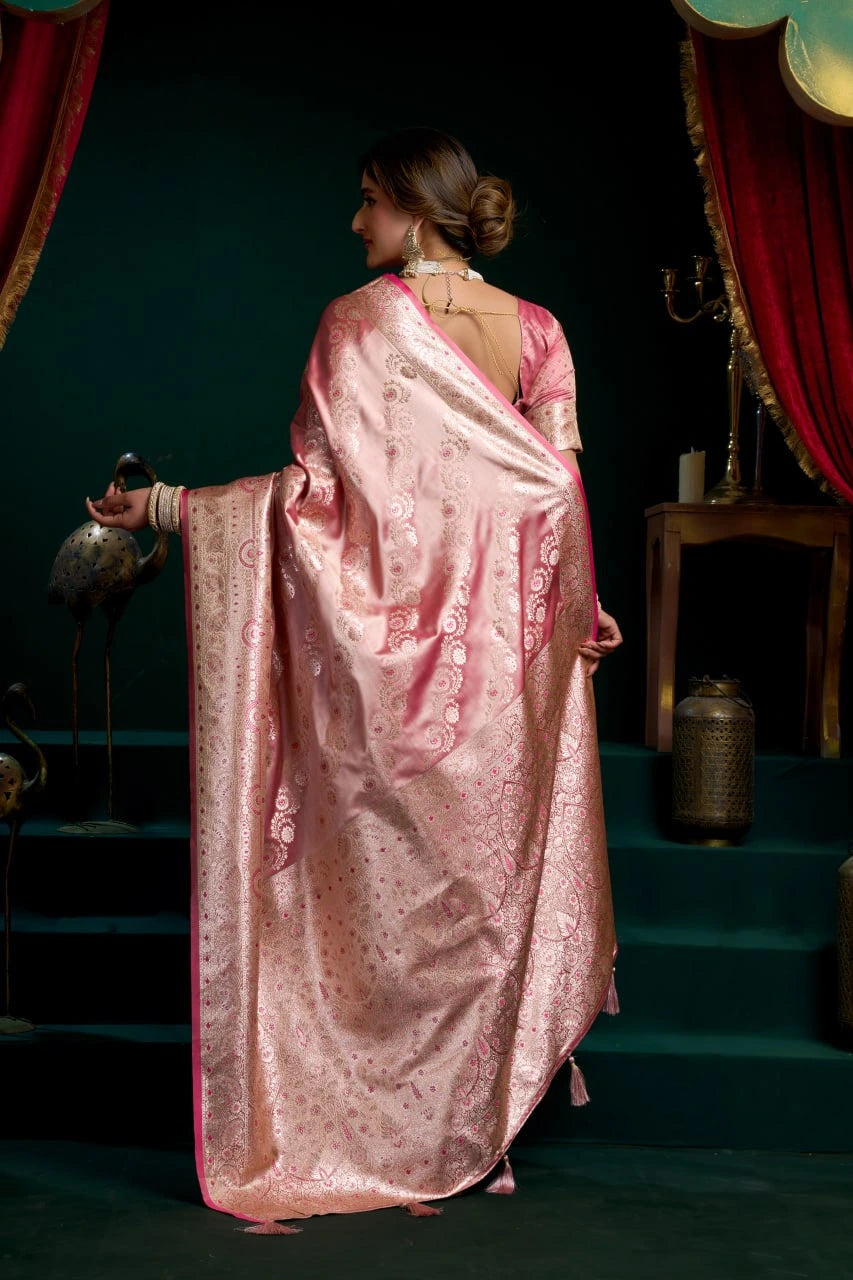Woman in a pink saree standing in a dimly lit room with red curtains.