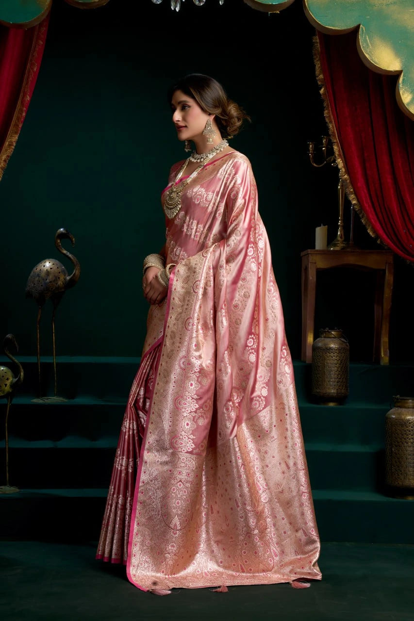 Woman in a traditional pink saree with gold patterns in a decorative setting.