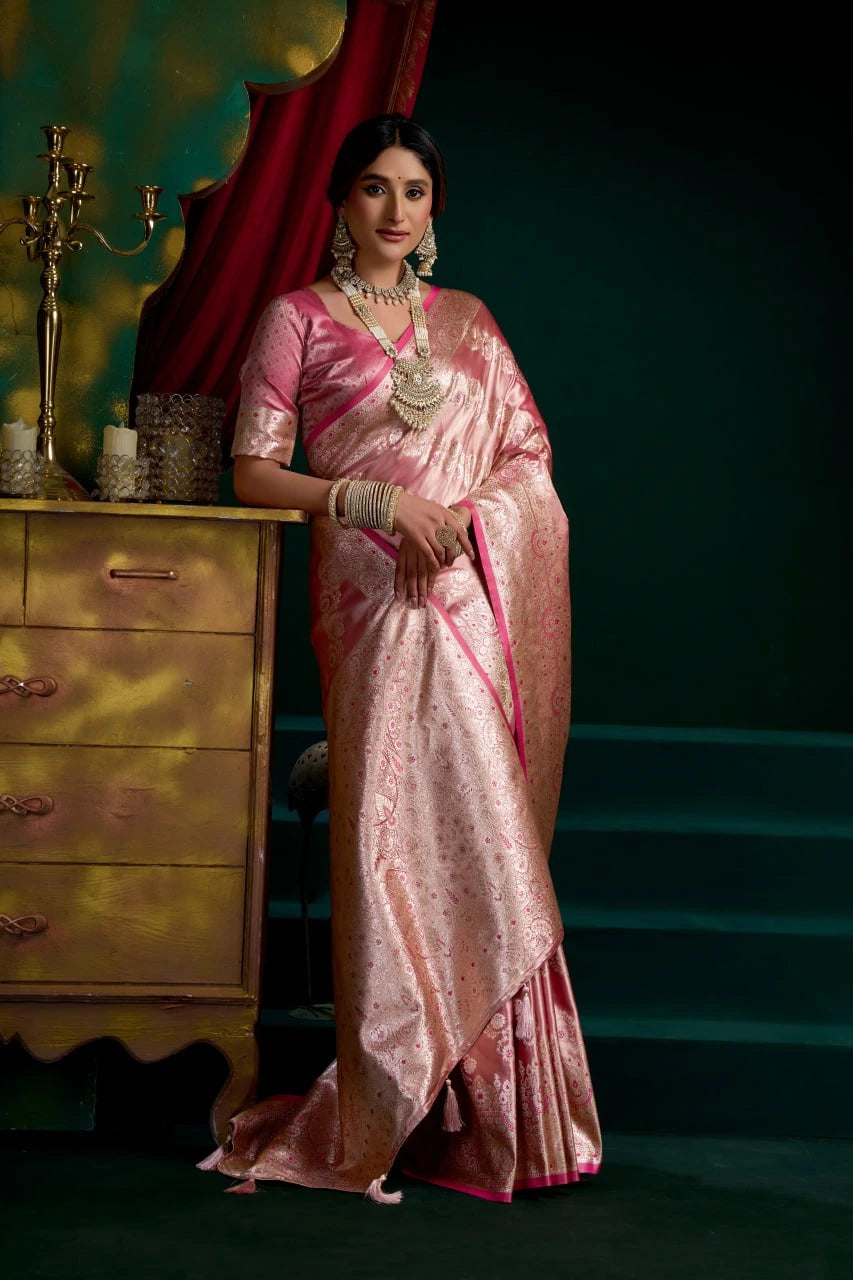 Woman in a pink saree standing in front of a decorative background with a yellow cabinet.