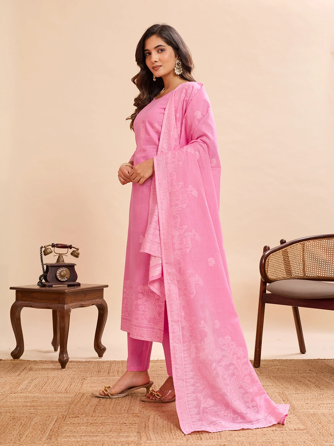 Woman in a pink traditional outfit standing in a room with a vintage phone and chair.