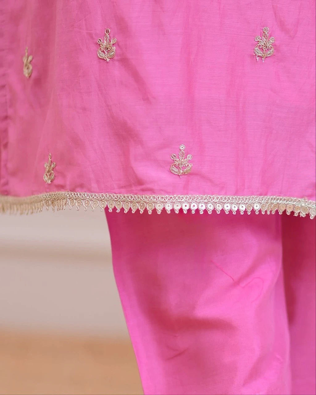 Pink fabric with gold embroidery and a decorative border on a white background