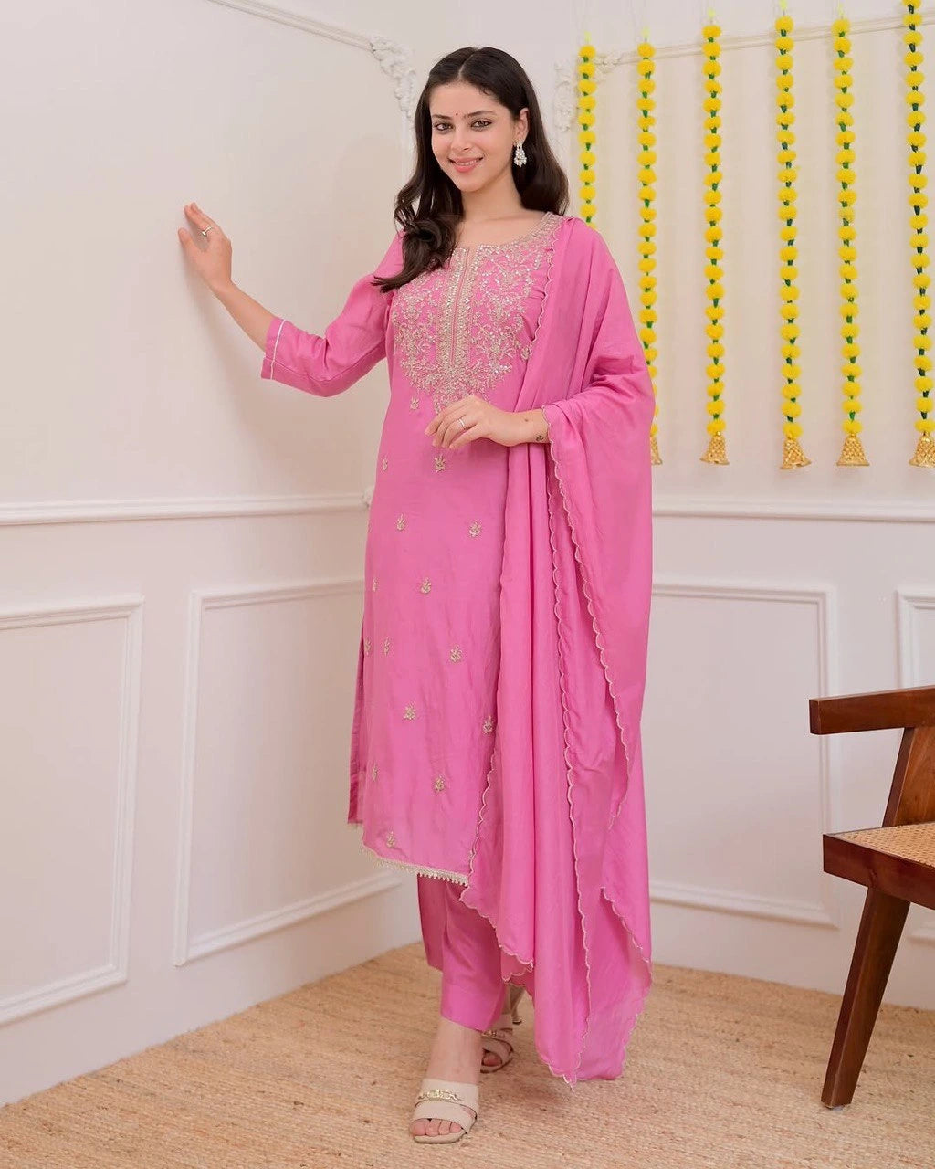 Woman in a pink traditional outfit standing in a room with decorative elements.