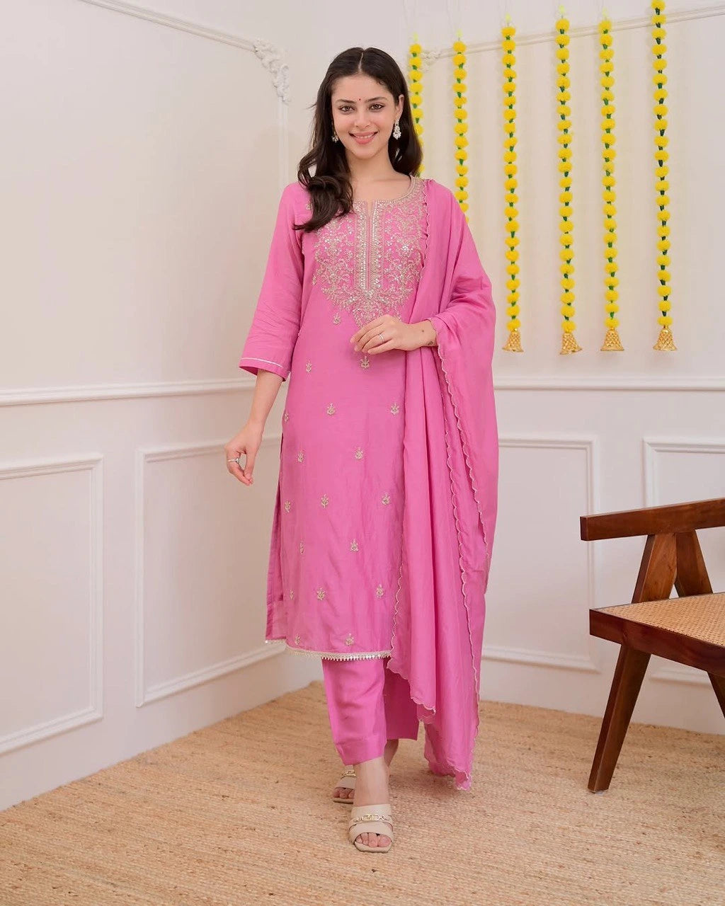 Woman in a pink traditional outfit standing in a room with decorative elements.