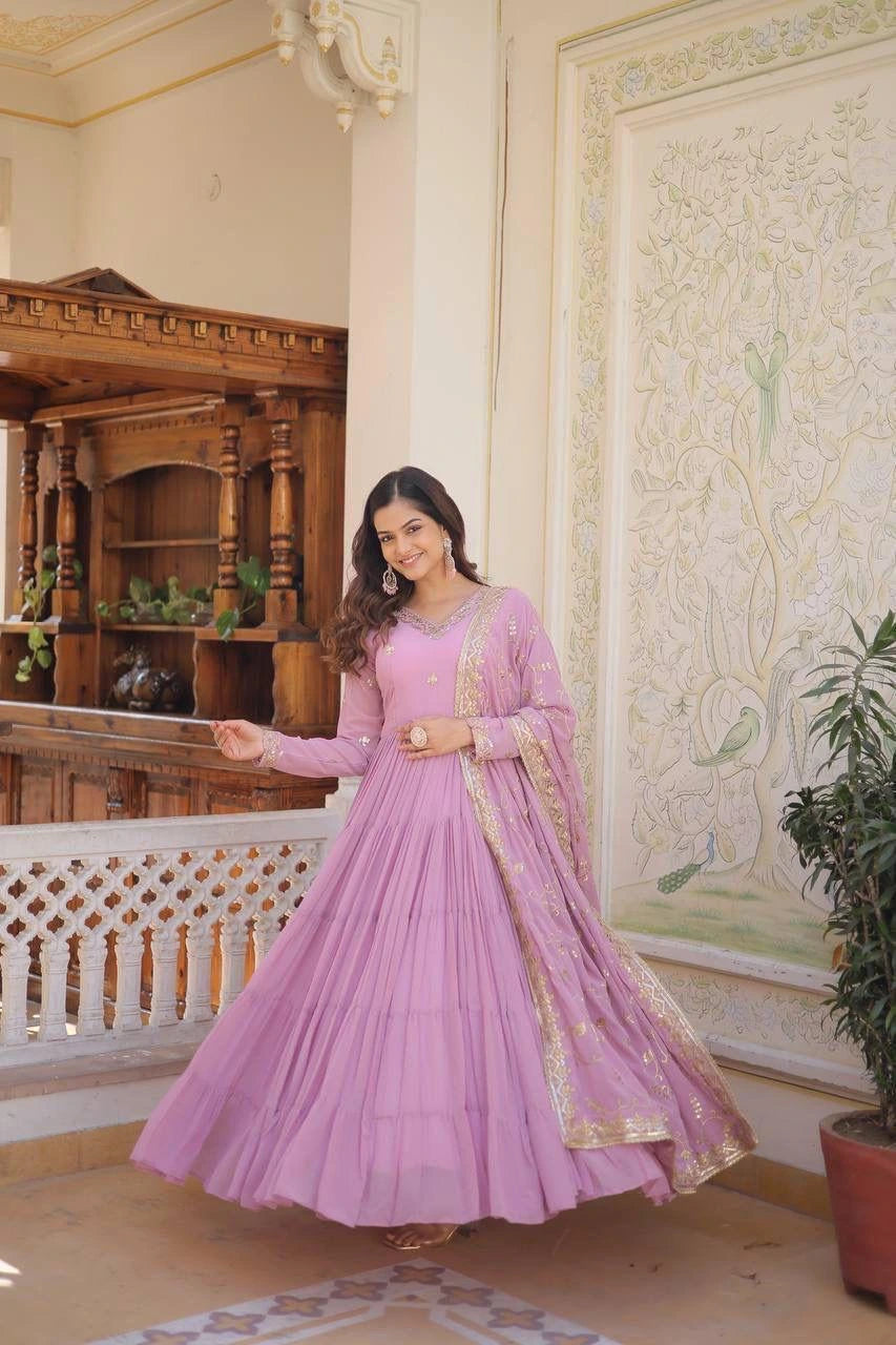 Woman in a pink traditional outfit standing in an ornate room with wooden decor and decorative wall.