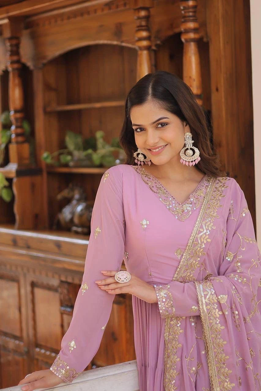 Woman in a pink traditional outfit with gold embroidery standing in front of a wooden cabinet.