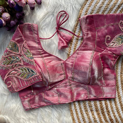 Pink embroidered blouse on a textured surface with flowers in the background